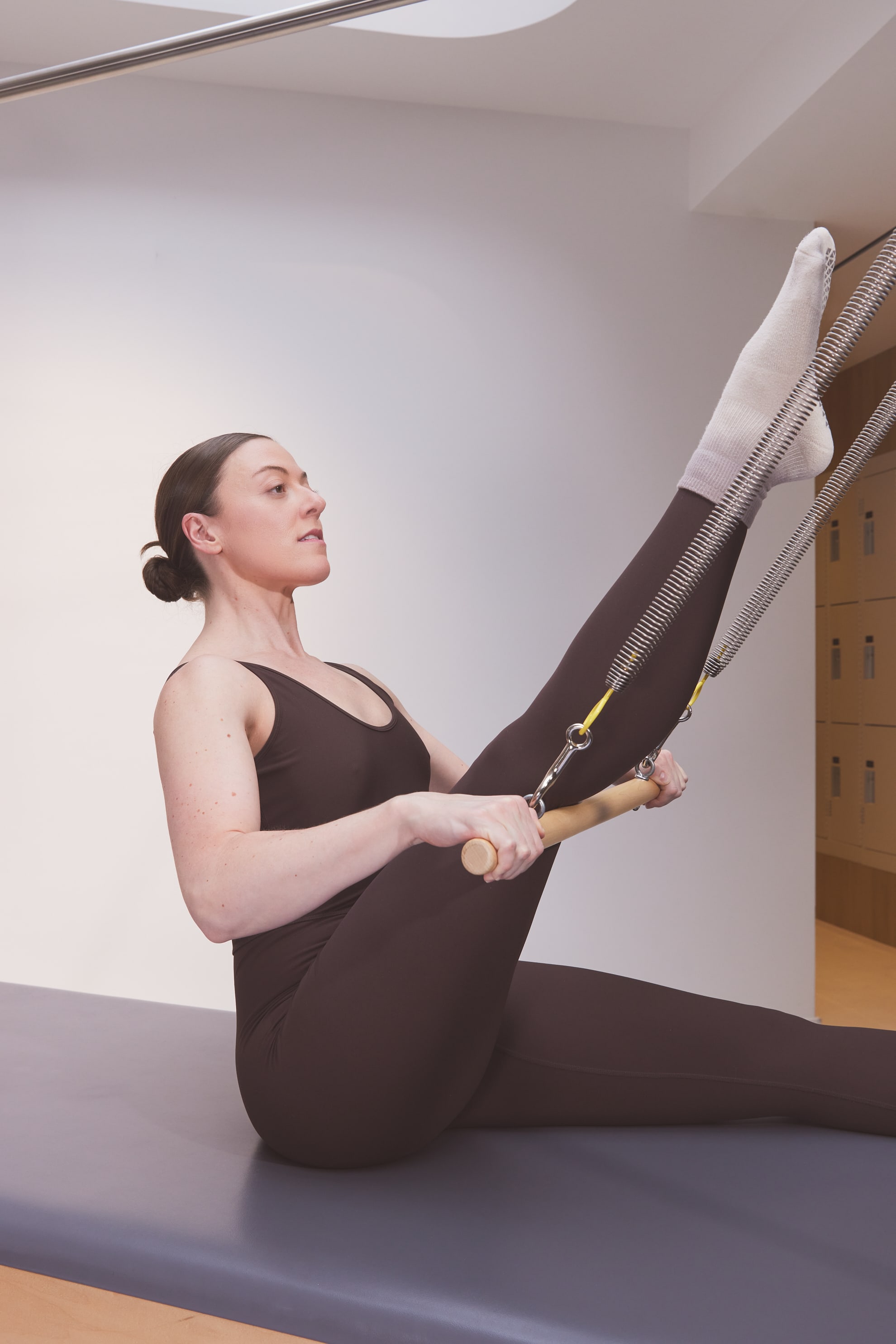A client practicing on the Cadillac with leg raised and supported by the push-through bar springs