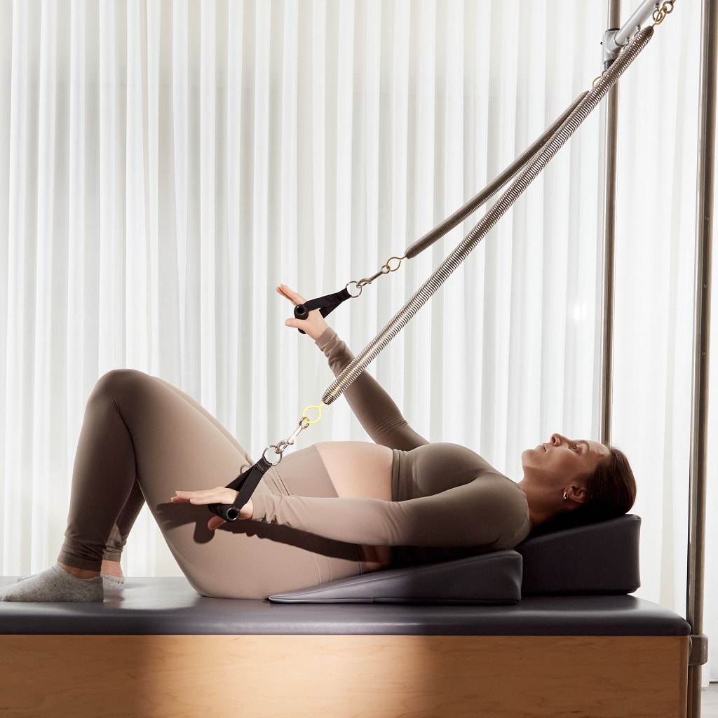 A pregnant client exercising on the Cadillac apparatus with supportive wedge and spring resistance at MTLPILATES