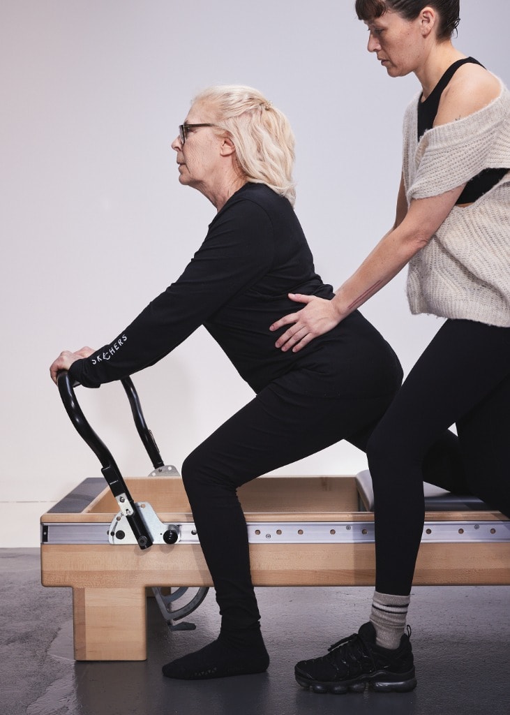 An instructor providing hands-on guidance to a client on the Reformer during a Slow Aging class at MTLPILATES